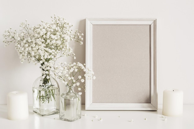 Bougies, fleurs de gypsophile et cadre photo sur fond de mur de table. Maquette vue de face.