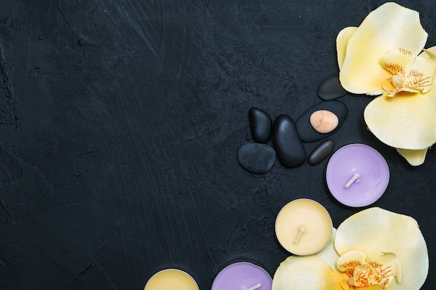 Photo bougies, fleurs d'orchidées et galets sur fond de pierre noire. vue de dessus, copiez l'espace. concept de spa, pose à plat.