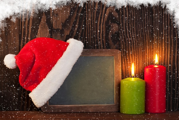 Photo bougies de noël et tableau noir avec chapeau de père noël dans la neige vue avec espace de copie