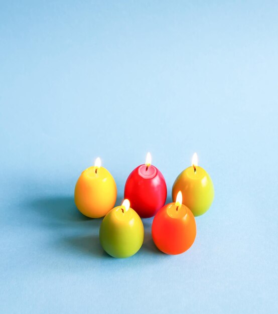 Bougies de paraffine brûlantes lumineuses en forme d'oeufs de Pâques colorés sur fond bleu.