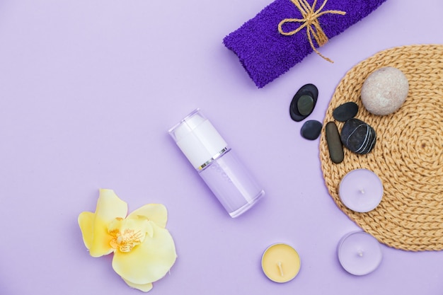 Bougies parfumées, serviette, lotion et cailloux sur fond lilas. Vue de dessus, espace de copie, mise à plat. Concept de spa et de soins du corps.