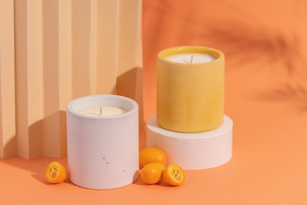 Bougies de soja aromatiques de qualité supérieure dans un pot en béton gris sur fond orange avec des fruits orange et de l'ombre