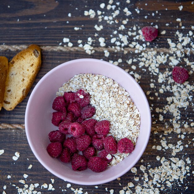 Bouillie d'avoine avec framboises et toasts sur fond noir. Mode de vie sain. Respectueux de la nature. Des granules d'avoine sont dispersés autour.