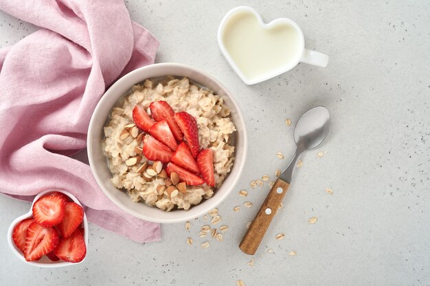 Bouillie d'avoine avec tranches de fraises, noix, amandes et miel dans un bol bleu sur une table grise. Alimentation saine, régimes amaigrissants, concept de nourriture végétarienne. Place pour le texte