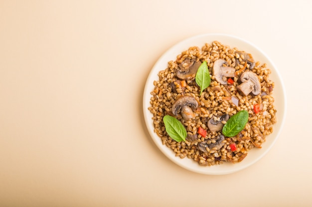 Bouillie d'épeautre (blé dinkel) avec des légumes et des champignons sur une plaque en céramique sur fond orange. Vue de dessus, espace copie.