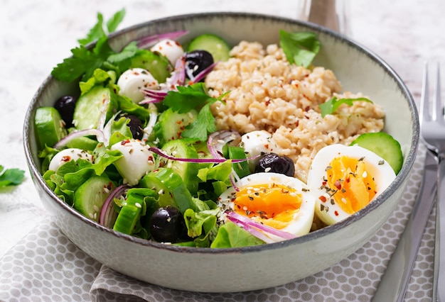 Bouillie de flocons d'avoine pour le petit-déjeuner avec des œufs durs, du fromage mozzarella au concombre et des herbes vertes Des aliments sains et équilibrés