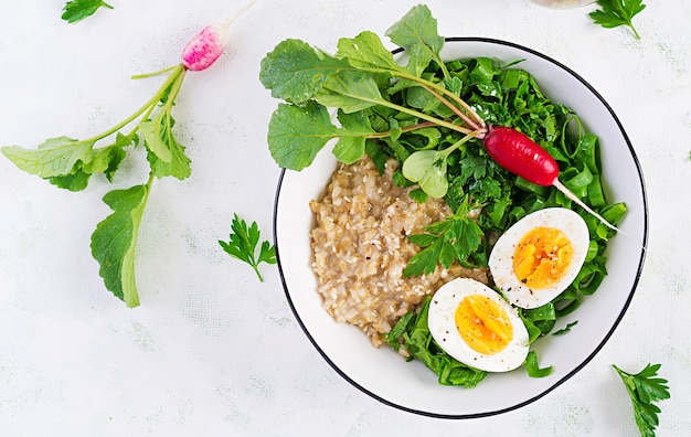 Bouillie de flocons d'avoine pour le petit-déjeuner avec des œufs durs, des radis et des herbes vertes. Alimentation saine et équilibrée. Vue de dessus, ci-dessus