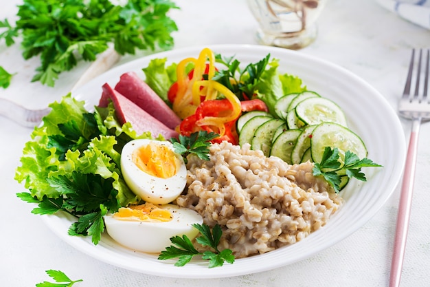 Bouillie de flocons d'avoine pour le petit-déjeuner avec salade d'œufs à la coque, jambon et légumes. La nourriture saine.