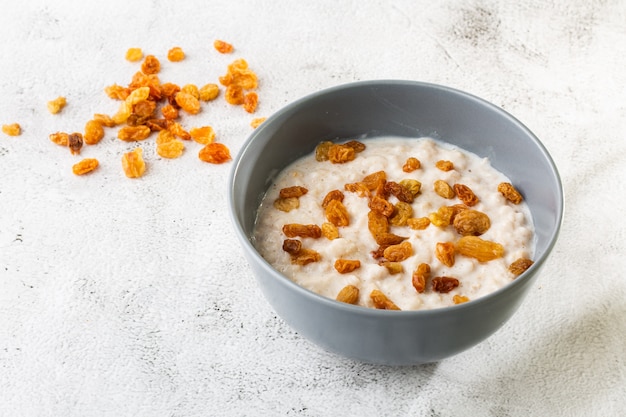 Bouillie de gruau ou gruau d'avoine ou céréales de petit déjeuner avec des raisins secs isolés sur fond de marbre blanc. Nourriture faite maison. Petit déjeuner savoureux. Mise au point sélective. Photo horizontale.