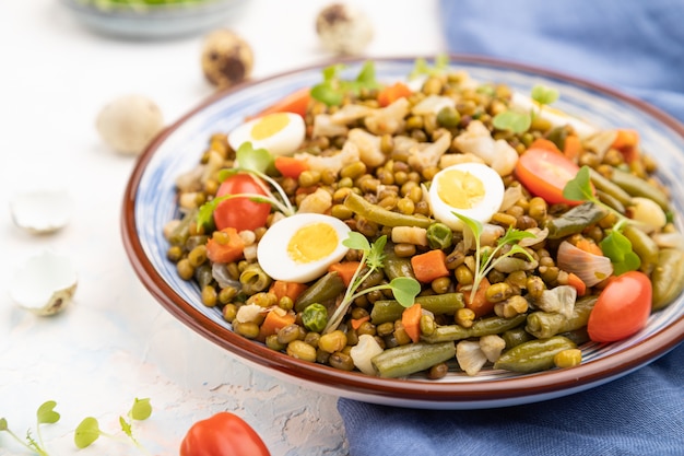 Bouillie de haricot mungo avec des œufs de caille, des tomates et des germes micro-verts sur un fond de béton blanc.