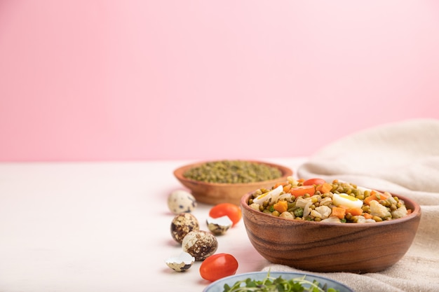 Bouillie de haricots mungo aux œufs de caille, tomates et pousses microgreen sur fond blanc et rose et textile en lin.