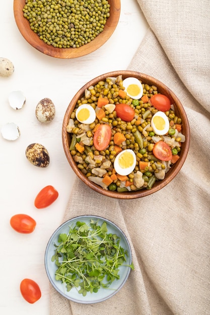 Bouillie de haricots mungo avec des œufs de caille, des tomates et des germes de micro-vert sur fond de bois blanc et textile en lin. Vue de dessus, mise à plat, gros plan.