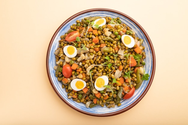 Bouillie de haricots mungo avec œufs de caille, tomates et pousses microgreen sur une table orange pastel. Vue de dessus, gros plan.