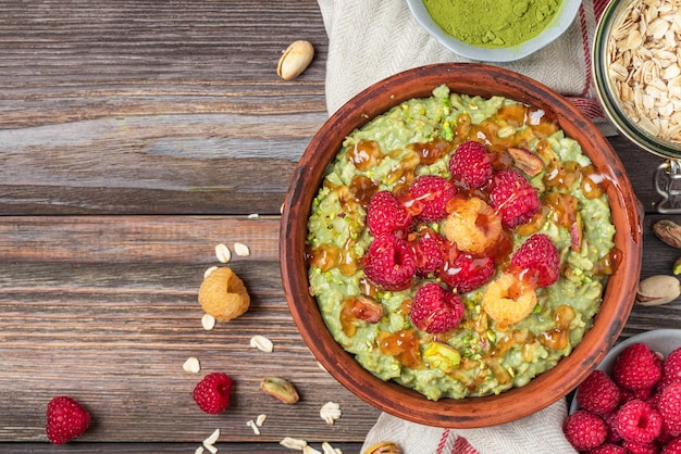 Bouillie de matcha à l'avoine avec sauce au caramel de framboises fraîches et pistaches dans un bol sur une table en bois rustique Vue de dessus