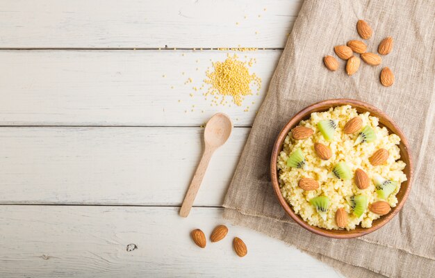 Bouillie de millet au kiwi et aux amandes dans un bol en bois sur un fond en bois blanc. Vue de dessus, espace copie.