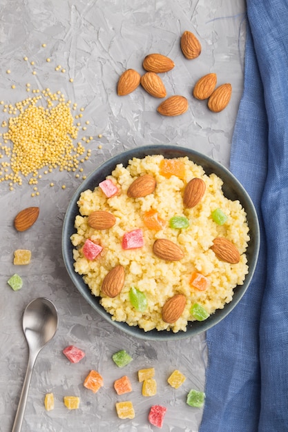 Bouillie de millet aux fruits confits et aux amandes dans un bol en céramique bleu sur fond de béton gris. Vue de dessus, gros plan.