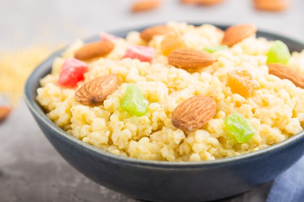 Bouillie de millet aux fruits confits et aux amandes dans un bol en céramique bleue sur une surface en béton gris. Vue latérale, mise au point sélective.