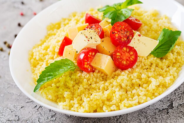 Bouillie de millet avec fromage, beurre et basilic dans un bol blanc. Nourriture savoureuse. Petit déjeuner.