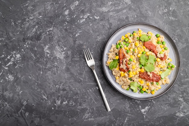 Bouillie de quinoa aux pois verts, maïs et tomates séchées sur plaque en céramique sur une table en béton gris. Vue de dessus, mise à plat, espace de copie.