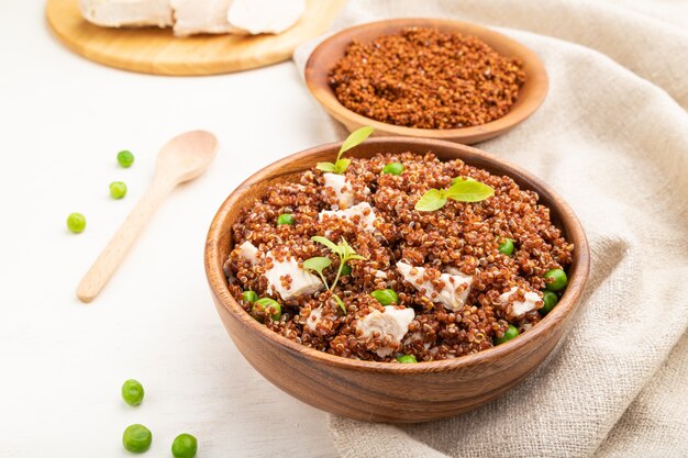 Bouillie de quinoa aux pois verts et poulet dans un bol en bois sur un fond en bois blanc.