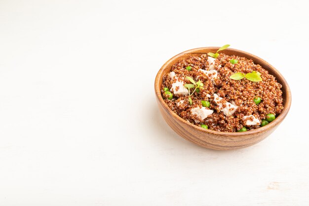 Bouillie de quinoa aux pois verts et poulet dans un bol en bois sur fond en bois blanc.