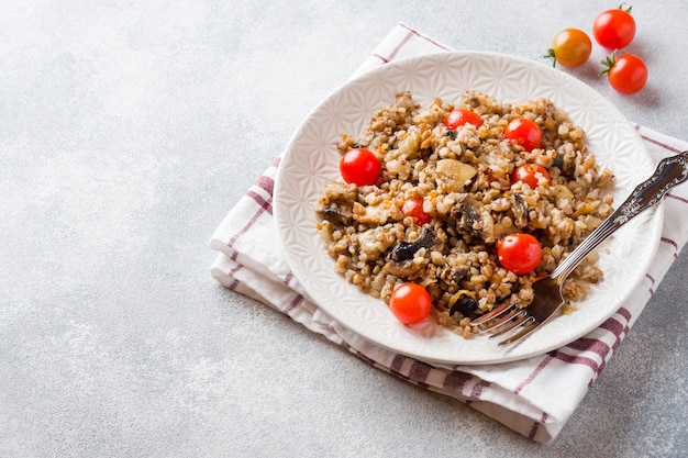 Bouillie de sarrasin aux champignons et tomates cerises sur une assiette. Espace de copie