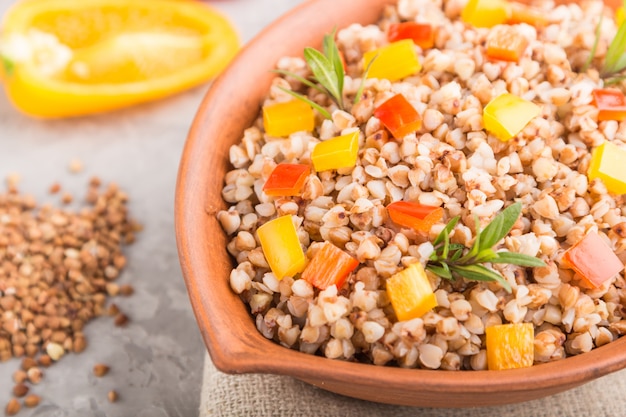 Bouillie de sarrasin aux légumes dans un bol en argile sur une surface en béton gris et textile en lin. Vue latérale, gros plan, mise au point sélective.