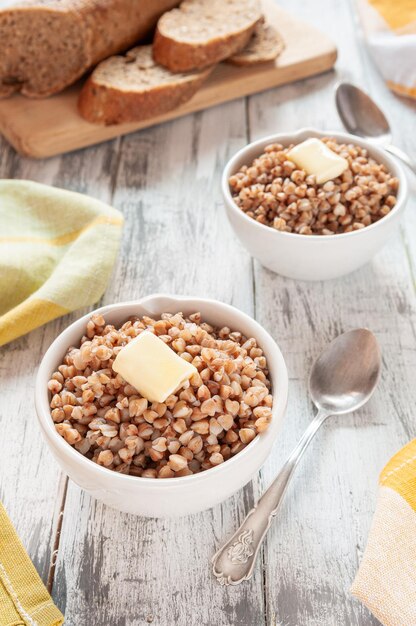 Bouillie de sarrasin bouillie dans des assiettes rondes blanches avec des tranches de beurre. au fond du pain de seigle. Sur un fond en bois clair.