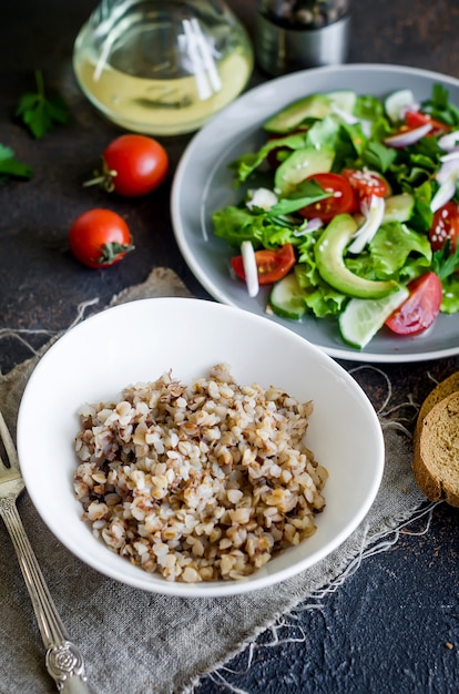 Bouillie de sarrasin chaude avec du beurre fondant dans une assiette et salade végétarienne saine de légumes frais pour le lanch sur table, vue de dessus, espace de copie Concept d'alimentation saine. Menu diététique