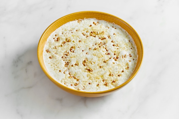 Bouillie de sarrasin cuit sur du lait dans un bol jaune vif sur un marbre clair