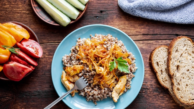 Bouillie de sarrasin avec de la viande, des oignons et des carottes sur un fond en bois. Avec des légumes frais, des concombres et des tomates.