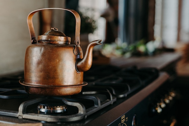 Bouilloire en bronze dans la cuisine moderne. Ancienne théière vintage sur cuisinière à gaz. Préparation du thé. Bouilloire en aluminium. Lumière du jour ensoleillée depuis la fenêtre.