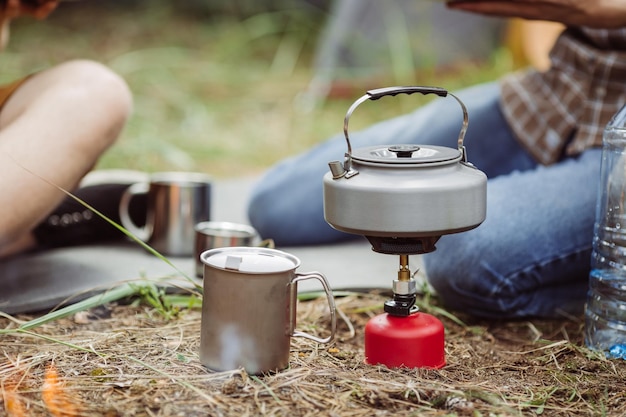 Une bouilloire sur un réchaud au propane à côté d'une tasse en métal