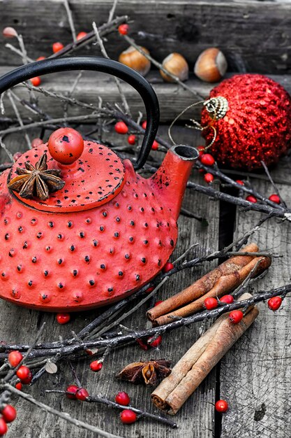 Bouilloire rouge, branches aux baies et bâtons de cannelle