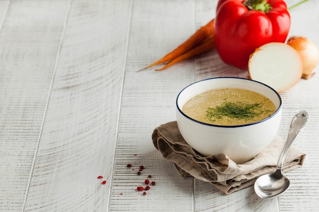 Bouillon fait maison dans un bol blanc sur une serviette à l'aneth et légumes frais sur un fond en bois. Le concept d'une alimentation saine. Copiez l'espace.