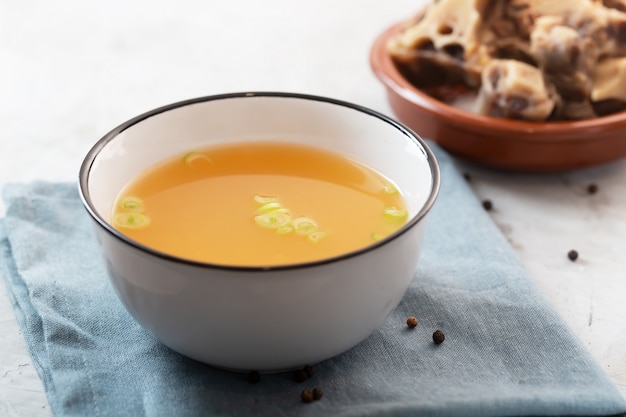 Bouillon d'os de boeuf fait maison dans un bol sur un espace en béton gris avec de la viande