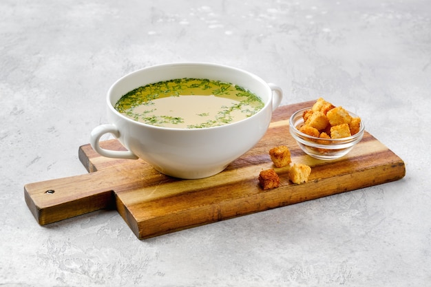 Bouillon de poulet avec croûtons sur planche de service en bois