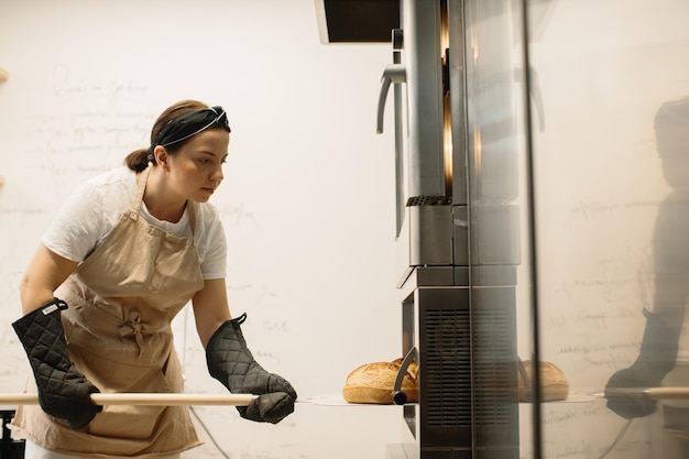 Boulanger femelle utilisant une peau pour sortir une miche de pain du four dans une boulangerie