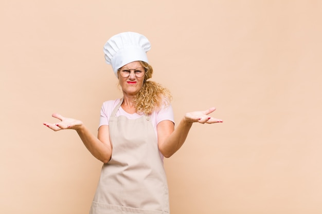 Boulanger femme d'âge moyen haussant les épaules avec une expression stupide, folle, confuse, perplexe, se sentant ennuyé et désemparé