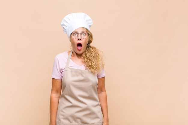 Boulanger de femme d'âge moyen se sentant terrifié et choqué, avec la bouche grande ouverte de surprise