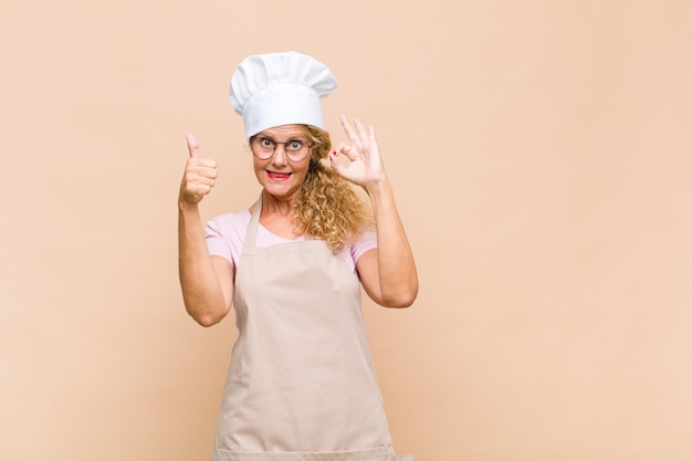 Boulanger de femme d'âge moyen se sentir heureux, étonné, satisfait et surpris, montrant bien et les pouces vers le haut des gestes, souriant