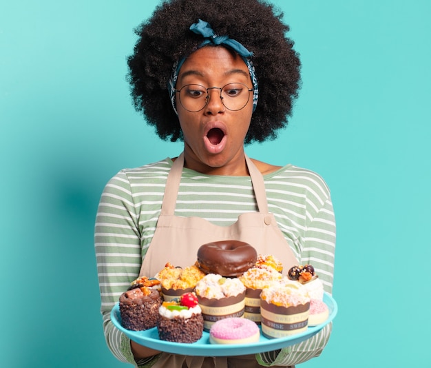 Boulanger de jeune jolie femme afro avec des gâteaux