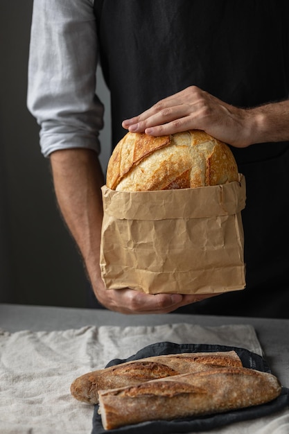 Un boulanger mâle européen adulte tient un pain frais rond dans ses mains un homme dans une boulangerie tient un