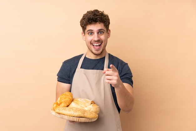 Boulanger mâle tenant une table avec plusieurs pains isolés sur le mur de points de doigt beige à vous