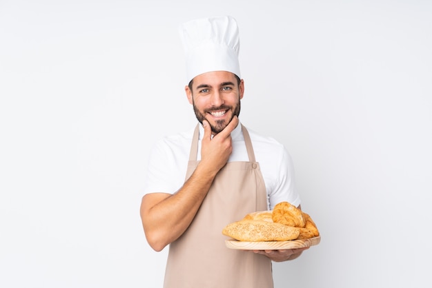 Boulanger mâle tenant une table avec plusieurs pains sur mur blanc en riant