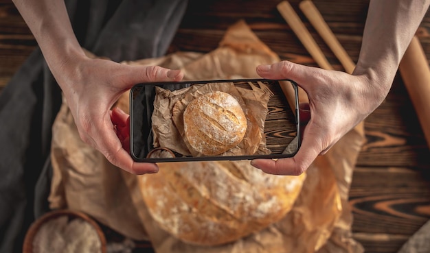 Un boulanger prend des photos de pain frais fait maison sur son téléphone pour un post sur les réseaux sociaux