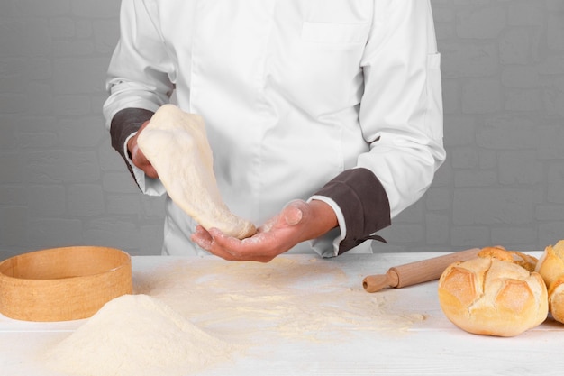 Un boulanger tenant de la pâte à pain dans ses mains à côté de pain de blé italien frais sur une table avec de la farine