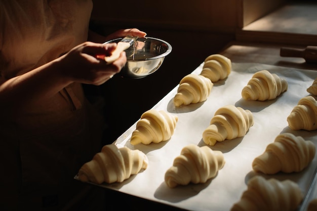 Une boulangère enduit des croissants crus avec un pinceau dans le jaune pendant le processus de cuisson