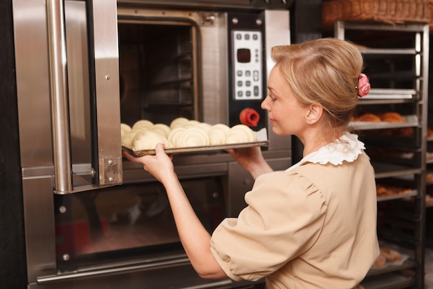 Boulangerie mettant des croissants crus au four dans sa boulangerie