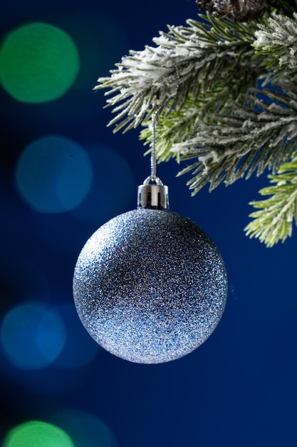 Boule bleue brillante sur une branche enneigée d'un arbre de Noël sur fond bleu